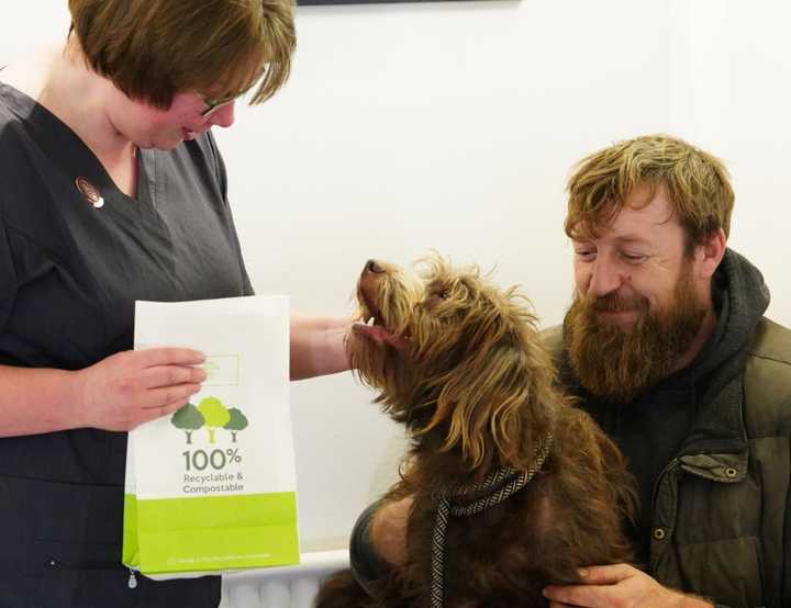 Veterinary nurse handing an eco friendly bag to a pet owner with a dog on his lap