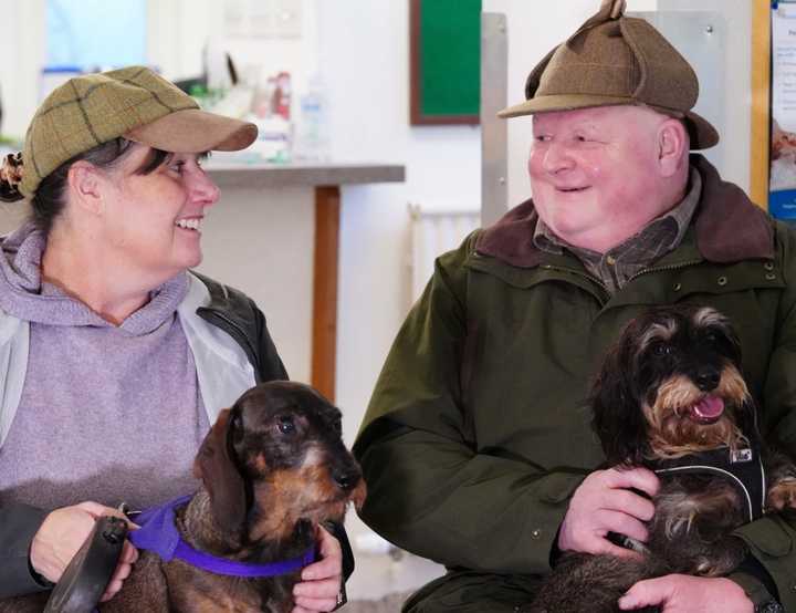 two pet owners smiling holding miniature dachshunds