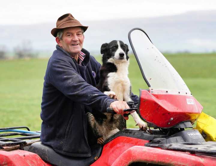 Farmer and his collie dog on a red quad bike in a field